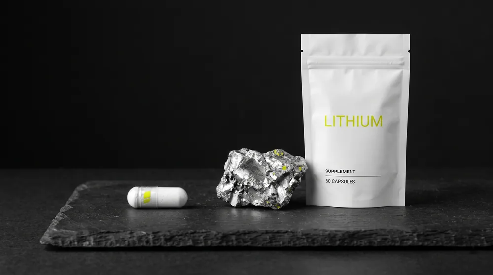 Reines Lithium-Element neben einer weißen Supplement-Kapsel auf dunklem Steinuntergrund
