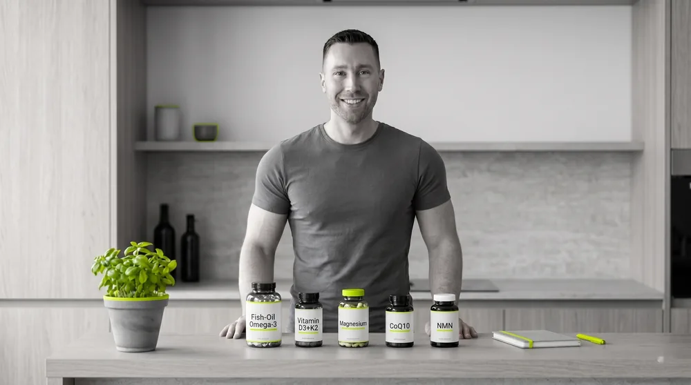 Nils in einer hellen Küche hinter seinem Longevity-Stack — Omega-3, Vitamin D3+K2, Magnesium, CoQ10 und NMN