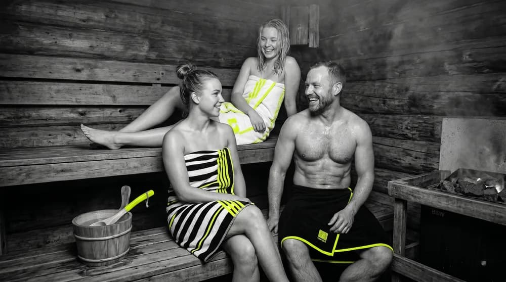 People relaxing in a Finnish wooden sauna with a water bucket and hot stones — regular heat as a cardiovascular longevity lever