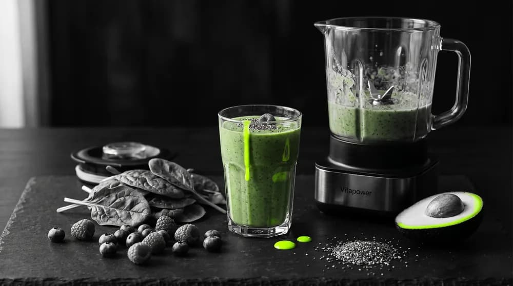 Smoothie verde con espinacas, bayas, semillas de chía y aguacate junto a una batidora de alta potencia en una encimera clara
