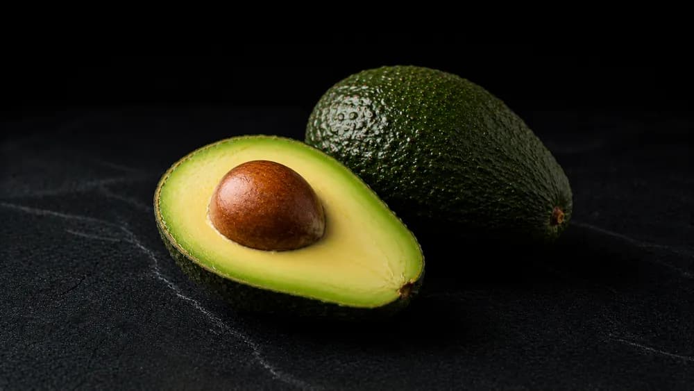 Halbierte Avocado mit Kern auf dunklem Steinuntergrund
