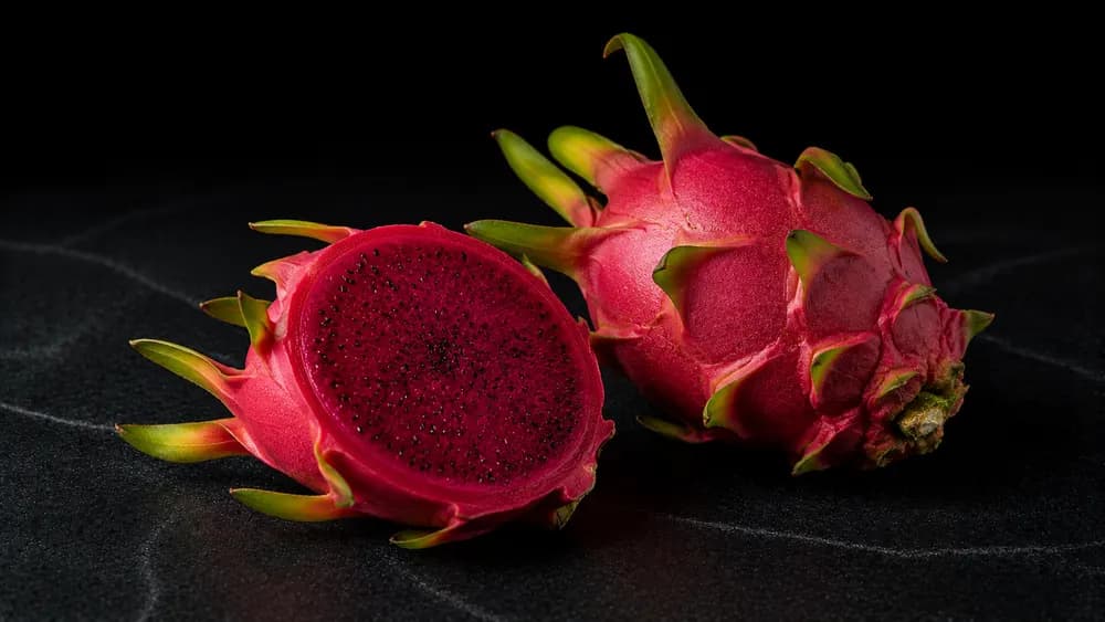 Aufgeschnittene Drachenfrucht mit rotem Fruchtfleisch auf dunklem Steinuntergrund