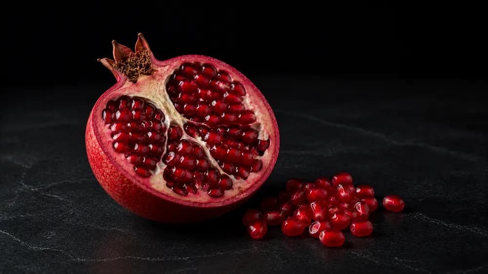 Aufgeschnittener Granatapfel mit Kernen auf dunklem Steinuntergrund
